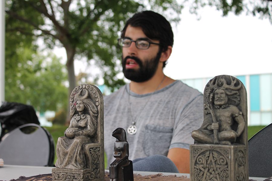 Michael David, part of the Wiccan Club sits at a club table in Falcon Square with artifacts. David created the club in hopes of spreading diversity and finding other people who practice the religion. Photo credit: Gustavo Lopez