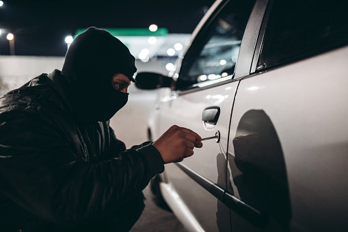 Caucasian man with ski mask stealing a car at night.