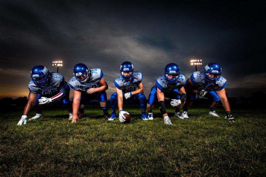 Football players in blue jersey-lined under Grey white cloudy sky during sunset. Players are ready for game time. Photo credit: Binyamin Mellish/Pexels.com