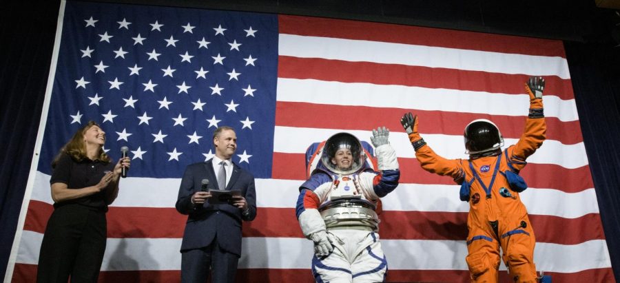 Amy+Ross%2C+a+spacesuit+engineer+at+NASA%E2%80%99s+Johnson+Space+Center%2C+left%2C+and+NASA+Administrator+Jim+Bridenstine%2C+second+from+left%2C+watch+as+Kristine+Davis%2C+a+spacesuit+engineer+at+NASA%E2%80%99s+Johnson+Space+Center%2C+wearing+a+ground+prototype+of+NASA%E2%80%99s+new+Exploration+Extravehicular+Mobility+Unit+%28xEMU%29%2C+and+Dustin+Gohmert%2C+Orion+Crew+Survival+Systems+Project+Manager+at+NASA%E2%80%99s+Johnson+Space+Center%2C+wearing+the+Orion+Crew+Survival+System+suit%2C+right%2C+wave+after+being+introduced+by+the+administrator%2C+Tuesday%2C+Oct.+15%2C+2019+at+NASA+Headquarters+in+Washington.+The+xEMU+suit+improves+on+the+suits+previous+worn+on+the+Moon+during+the+Apollo+era+and+those+currently+in+use+for+spacewalks+outside+the+International+Space+Station+and+will+be+worn+by+first+woman+and+next+man+as+they+explore+the+Moon+as+part+of+the+agency%E2%80%99s+Artemis+program.+The+Orion+suit+is+designed+for+a+custom+fit+and+incorporates+safety+technology+and+mobility+features+that+will+help+protect+astronauts+on+launch+day%2C+in+emergency+situations%2C+high-risk+parts+of+missions+near+the+Moon%2C+and+during+the+high-speed+return+to+Earth.+Photo+credit%3A+NASA%2FJoel+Kowsky