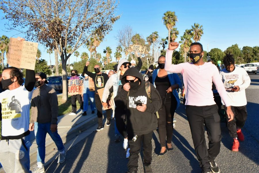 Dozens march through Marina Park in Long Beach to celebrate Black History Month. They raise their fists in solidarity with social reform groups who advocate for justice reform and the defunding of police.
