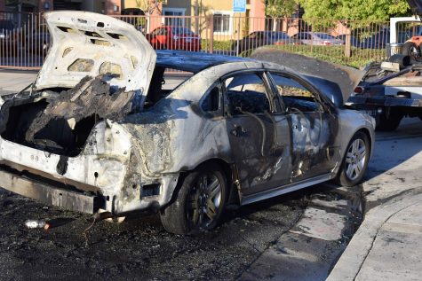 A Chevy sedan burns after a speaker in the trunk catches fire. The vehicle burns across the street from the Norwalk Town Square on April 29, 2021.