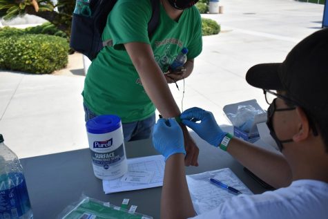 A Cerritos College student receives a wristband from Meximos Garcia at the health screening kiosk on Monday, Aug. 16, 2021. The wristband proves they have no COVID-19 symptoms, and they are safe to enter campus.