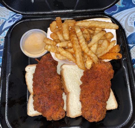 Dave's Hot Chicken tenders with a mild level spice placed on soft, white bread along with seasoned fries. To the left is the famous Dave's sauce.
