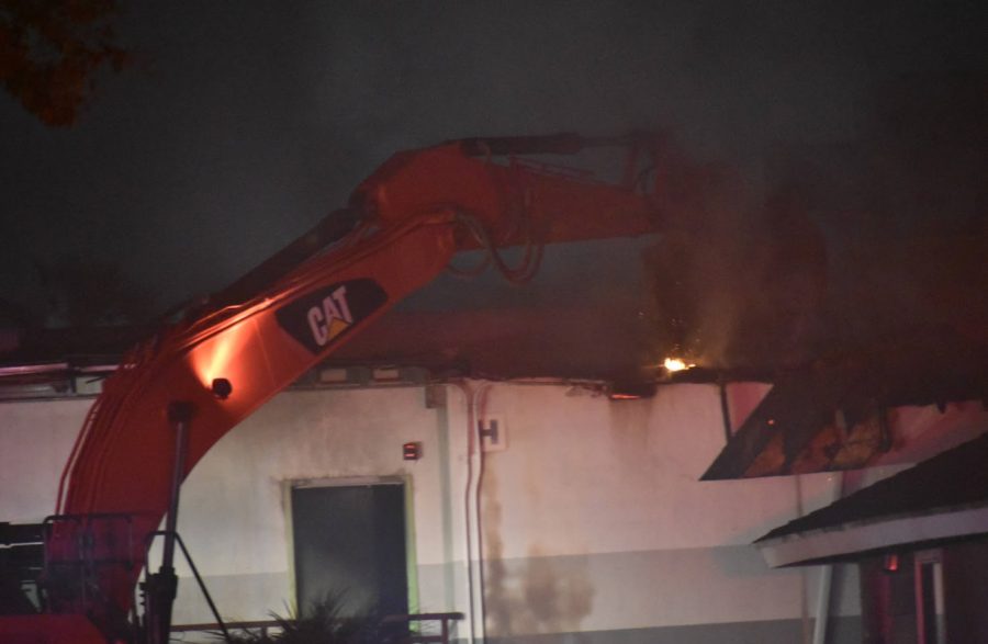 An excavator breaks in the roof of the burning storage facility. Fire crews worked  into the night to put out what remains of the fire on Nov. 9, 2021. 