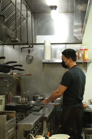 A Class 302 Cafe kitchen worker using utilities and tools to create food.