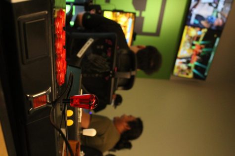 An arcade fight stick controller shown behind competitors. Players can also use handheld controllers.