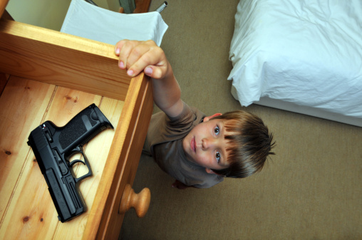 Boy (4-6 years old) reaching up to a bedroom drawer that contains a gun