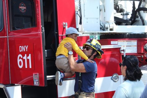 A firefighter lifts a boy up from the ground to help him sit in the firetruck.