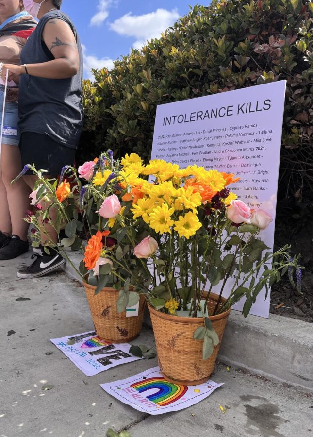 At the corner of Paramount Blvd and Imperial Hwy, a basket of flowers was set in front of a list of names of members of the LGBTQ+ community who have been murdered. Photo credit: Clarissa Arceo