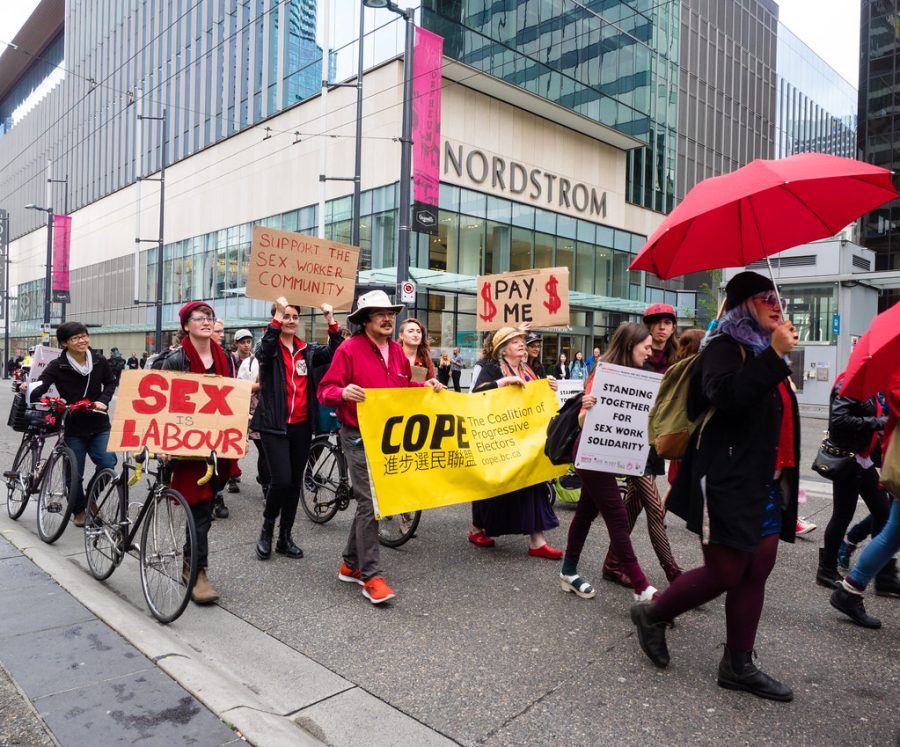 Protest in Canada taking place to stand up for sex workers. People marching down the street with signs and umbrellas. (2016) 