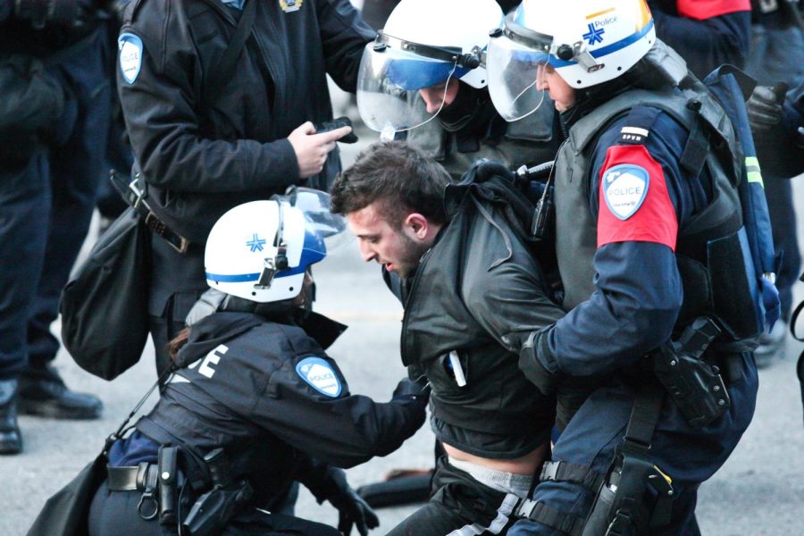 A man is getting arrested by one female and two male cops at a police brutality protest. 