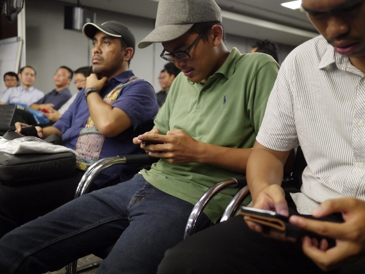 Men texting distracted by what is on their phones rather than listening to the seminar they are in.