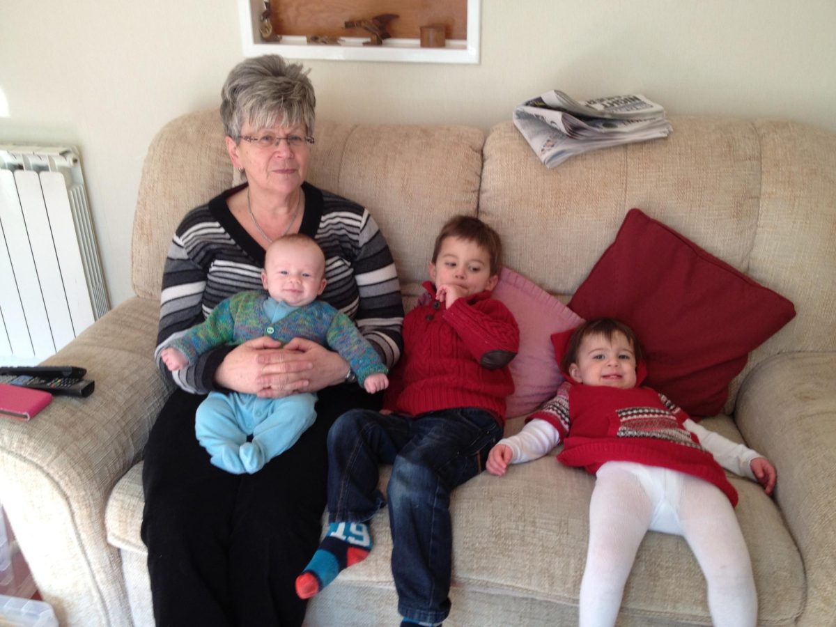 Grandma with her three grandchildren on the couch sitting down. 