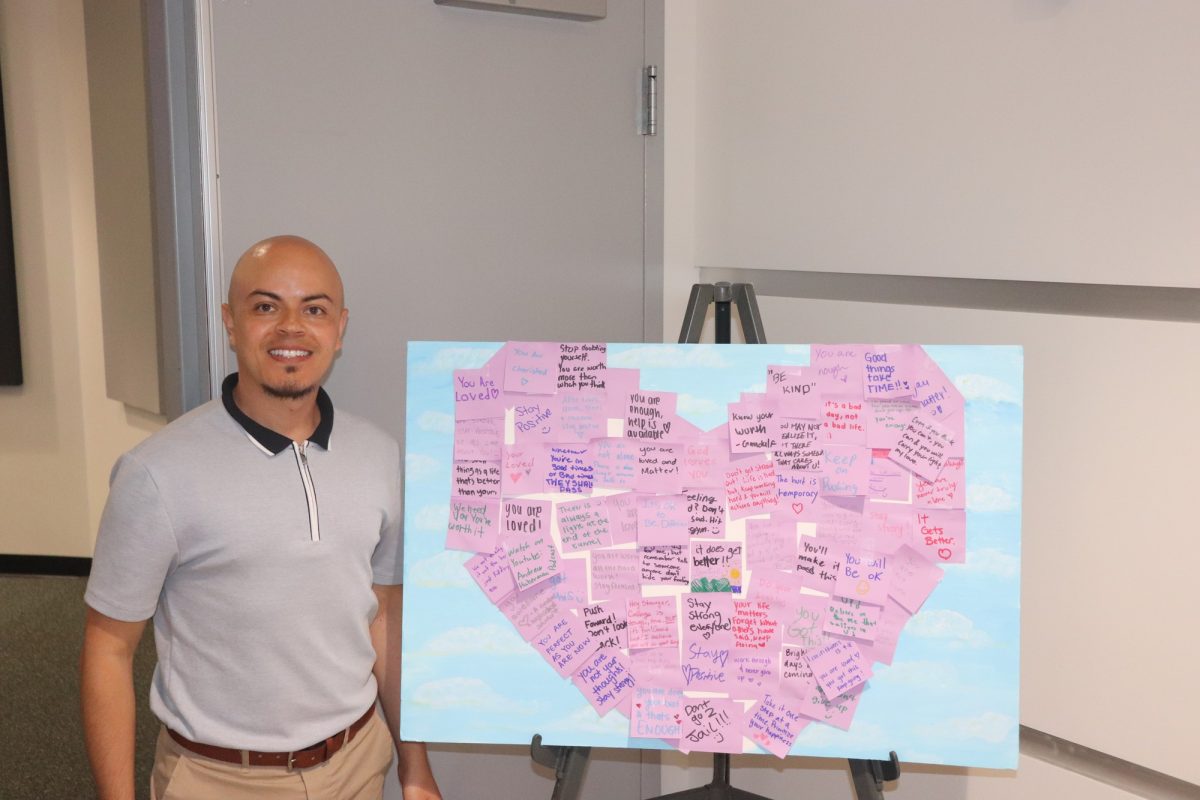 German Escobar with the Words of Encouragement board filled up by posted notes handwritten from students in the shape of a heart. 