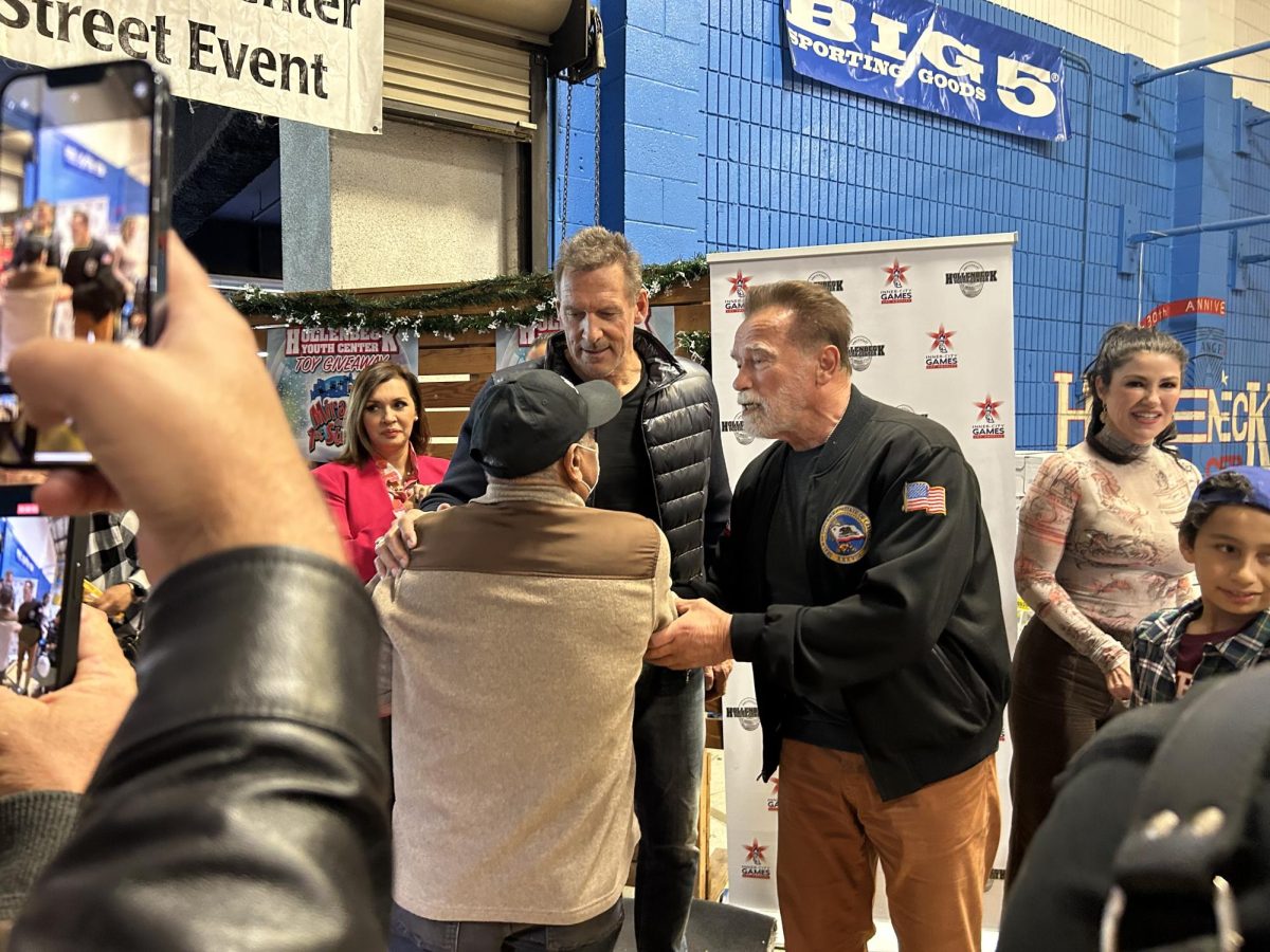 Ralf Moeller and Arnold Schwarzenegger shaking hands with a member of the community. 