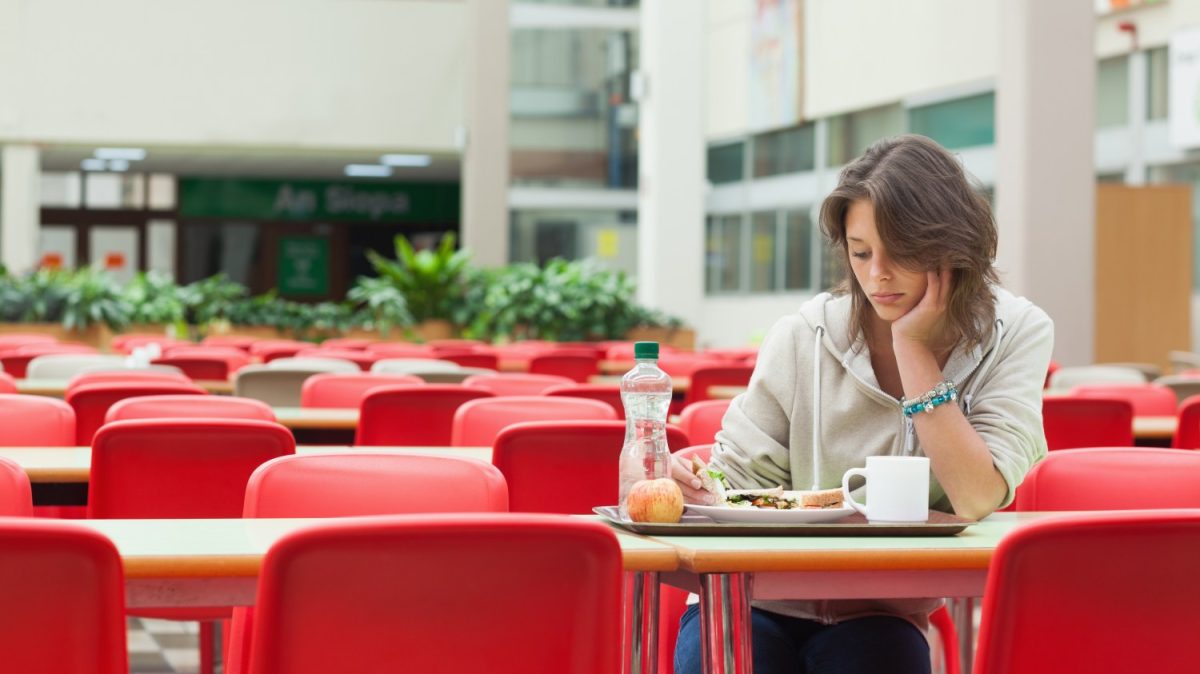 A student eats alone in a cafeteria. Photo credit: Alamy Stock Photo