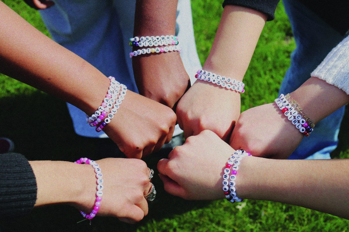 Six women wearing friendship bracelets joined in a circle. 