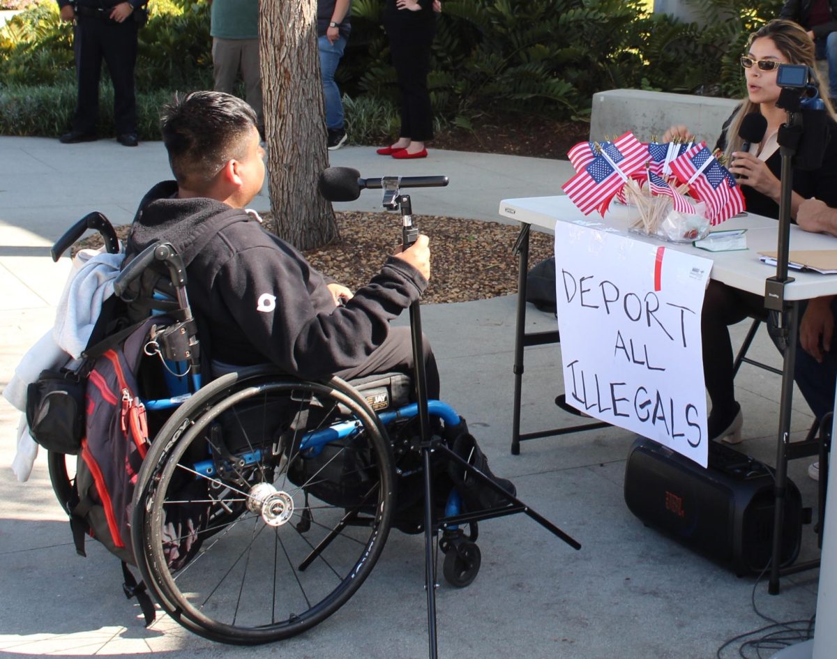 Araceli Martinez and J. Emilio Martinez sit at a table featuring a sign reading "DEPORT ALL ILLEGALS" while debating with Anson Z., whose full name has been withheld for his safety on March 9, 2026.