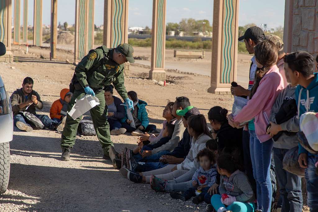 A U.S. Border Patrol agent detains migrants who turned themselves in after crossing the Rio Grande in El Paso. Photo credit: Mani Albrecht